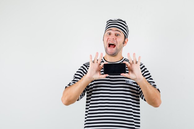 Young male taking photo on mobile phone in t-shirt, hat and looking glad , front view.