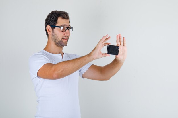 Young male taking photo on smartphone in white t-shirt