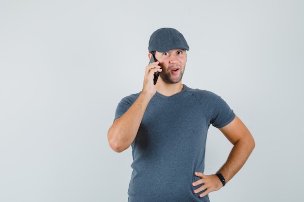 Young male talking on mobile phone in t-shirt cap and looking amazed