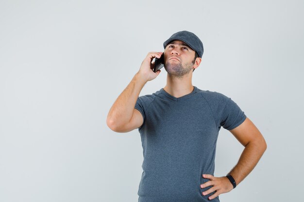 T- 셔츠 모자에 휴대 전화로 얘기하고 잠겨있는 찾고 젊은 남성