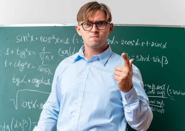 教室で数式を使って黒板の近くに立つ、不機嫌で怒っている眼鏡をかけた若い男性教師