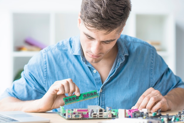 Young male technician fixing RAM in motherboard
