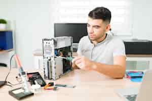 Free photo young male technician installing new components on a broken cpu for a customer. latin man running a repair shop