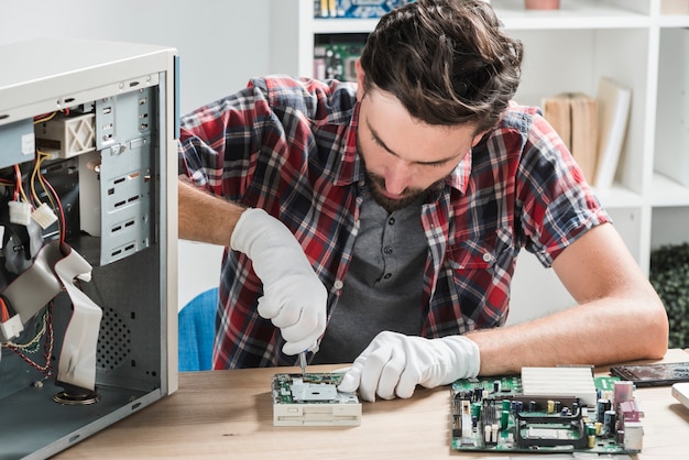 Young male technician wearing gloves fixing computer motherboard with screwdriver
