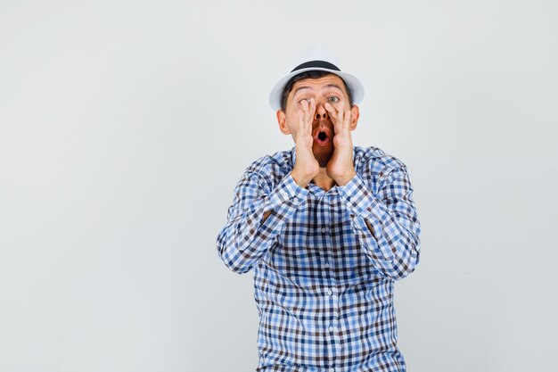 Young male telling secret with hands near mouth in checked shirt