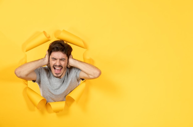 Young male thinking and looking from torn yellow paper background indoor guy facial