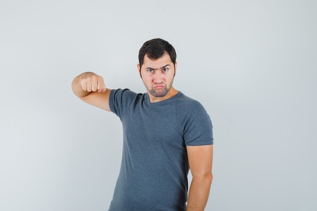 Молодой мужчина угрожает кулаком в серой футболке и выглядит нервным