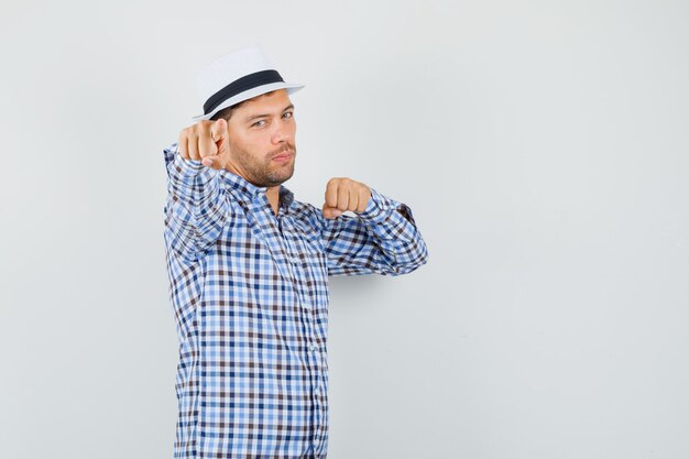 Young male threatening with fist while pointing at camera in checked shirt