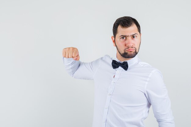 Young male threatening with fist in white shirt and looking furious. front view.