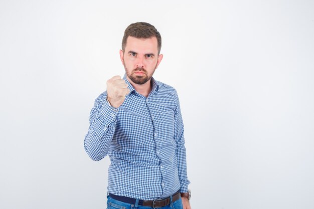 Young male threating with fist in shirt and looking serious , front view.