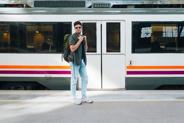 Бесплатное фото Молодой мужской турист с рюкзаком позирует на железнодорожной станции