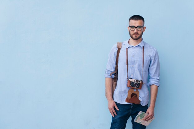 Young male traveler with camera around his neck standing near blue background