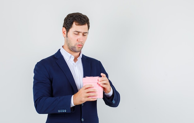 Young male trying to open gift box in suit and looking serious , front view.