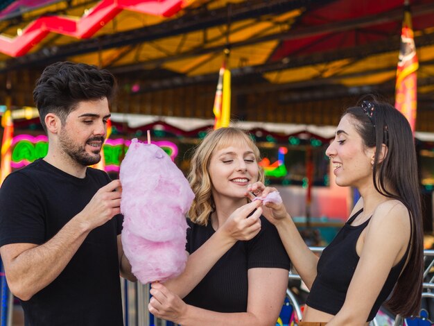 遊園地で綿菓子を食べる若い男性と2人の女性