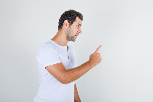 Young male warning somebody with gesture in white t-shirt and looking angry