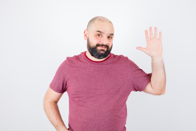 Young male waving hand for greeting in pink t-shirt , front view.