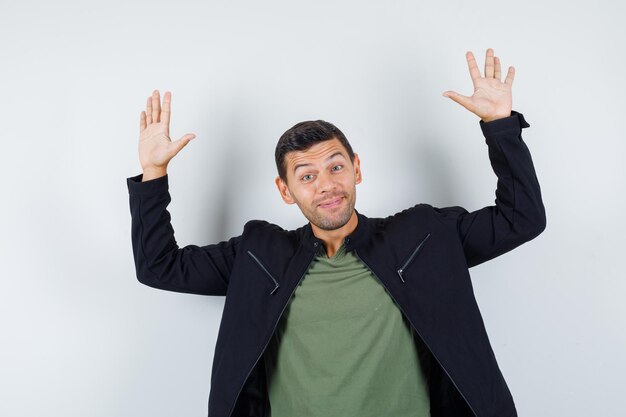 Young male waving hands to say goodbye in t-shirt, jacket and looking cheerful. front view.