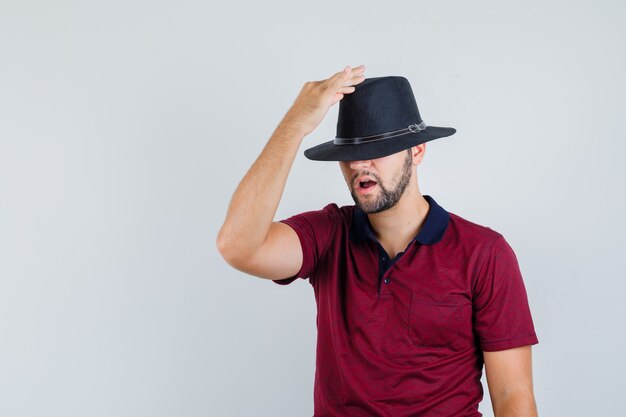 Young male wearing his hat in red t-shirt and looking weird. front view.