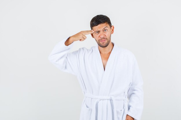 Young male in white bathrobe making suicide gesture , front view.