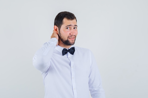 Young male in white shirt holding hand on neck and looking elegant , front view.