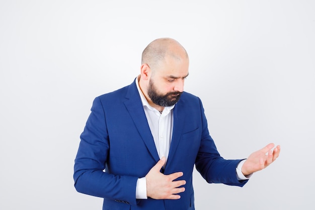 Young male in white shirt, jacket looking at his empty palm and looking sad , front view.