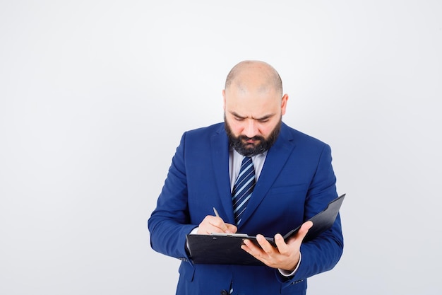 Young male in white shirt, jacket taking notes on clipboard and looking busy , front view.