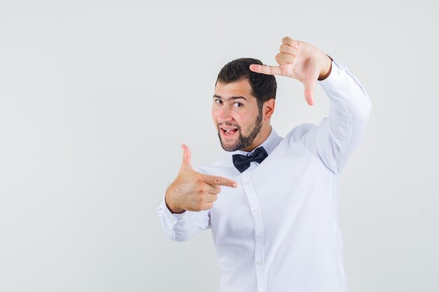 Young male in white shirt making frame gesture and looking cheerful , front view.