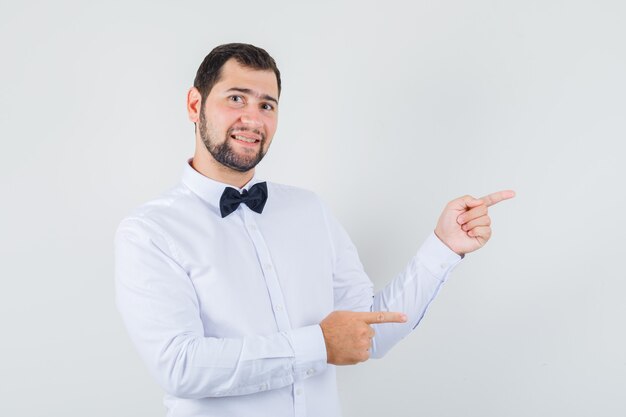 Young male in white shirt pointing to the side and looking cheery , front view.