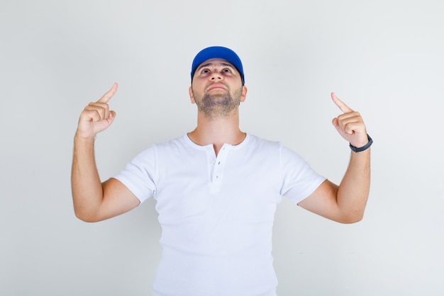 Молодой мужчина в белой футболке, синяя кепка, направленная вверх пальцами