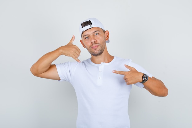 Free photo young male in white t-shirt, cap doing call me gesture with hands, front view.