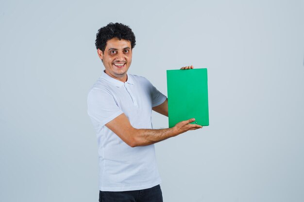 Young male in white t-shirt, pants holding clipboard and looking cheerful , front view.