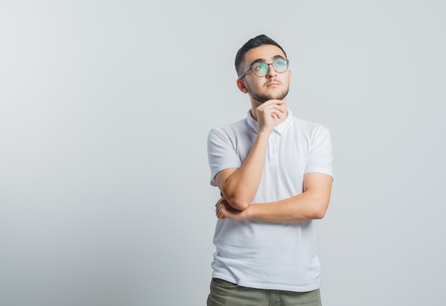 Young male in white t-shirt, pants propping chin on hand and looking pensive