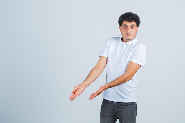 Young male in white t-shirt, pants showing something below and looking confused , front view.