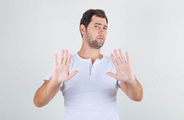 Young male in white t-shirt showing no sign and looking disgusted