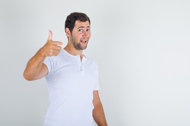 Young male in white t-shirt showing thumb up and smiling and looking pleased