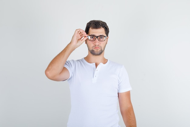 Young male in white t-shirt standing with hand on glasses