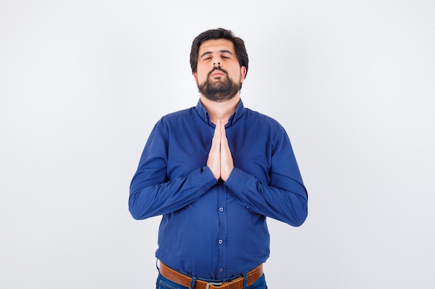 Young male wishing in royal blue shirt and looking hopeful , front view.