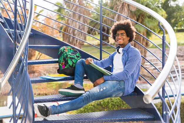 Young male with book and bags relaxing on the blue staircase in the park