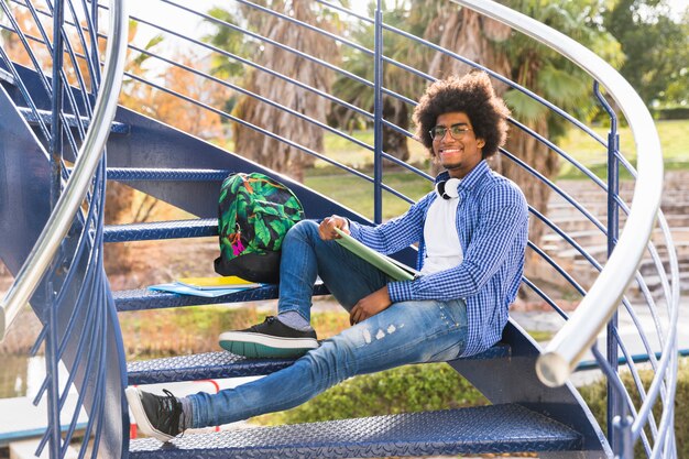 Молодой мужчина с книгой и сумки, расслабляющий на синей лестнице в парке