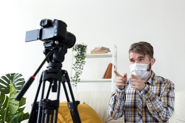 Young male with face mask recording video at home