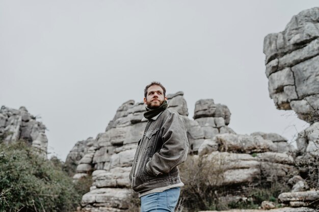 Young male with a jacket standing near rocky cliffs looking aside