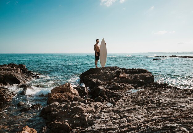 しぶき海の近くのサーフボードを持つ若い男性