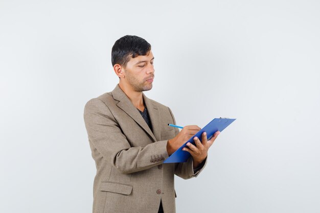 Young male writing something in grayish brown jacket,black shirt and looking intelligent , front view.