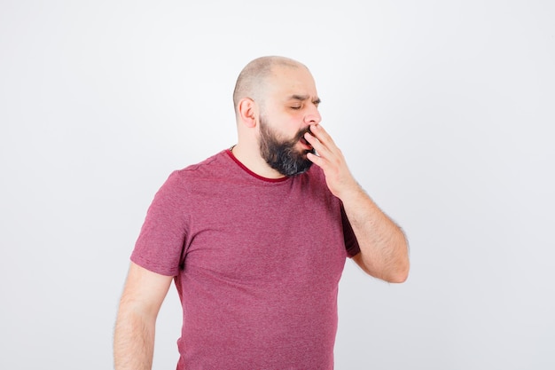 Young male yawning in pink t-shirt and looking sleepy. front view.