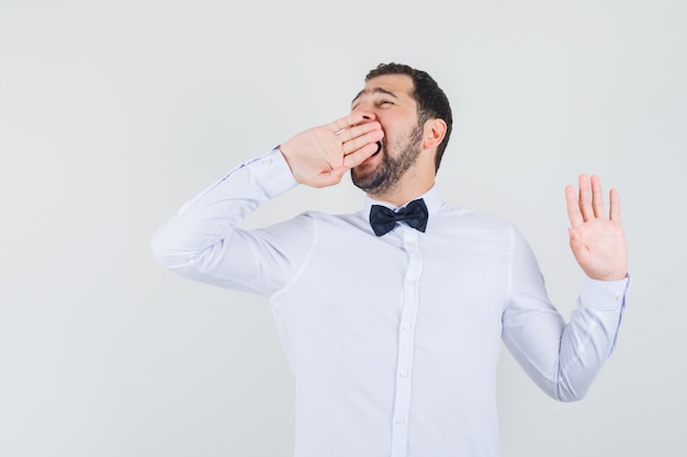 Young male yawning and stretching in white shirt and looking sleepy. front view.