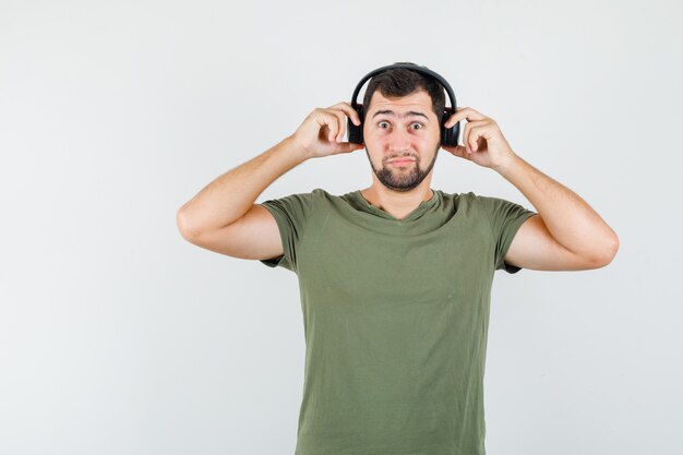 Young man adjusting headphones in green t-shirt and looking puzzled