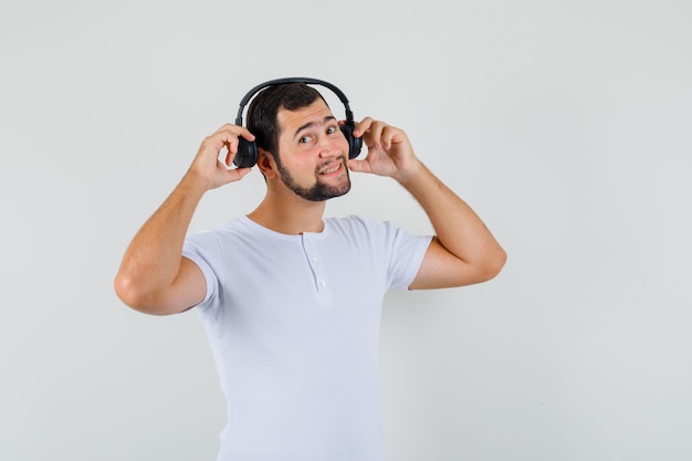 Young man adjusting headphones in white t-shirt and looking merry. front view.