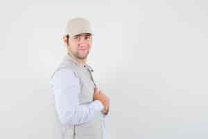 Free photo young man adjusting his collar in shirt,sleeveless jacket,cap and looking self-confident. .