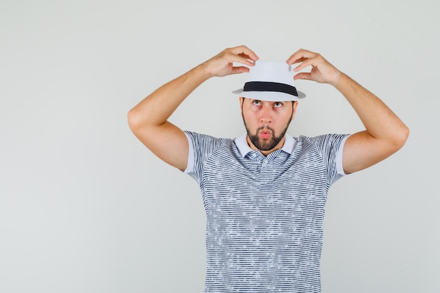 Foto gratuita giovane che si aggiusta il cappello mentre guarda in t-shirt, vista frontale.