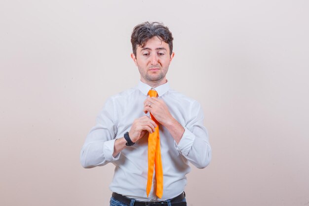 Young man adjusting his tie in shirt, jeans and looking discontent